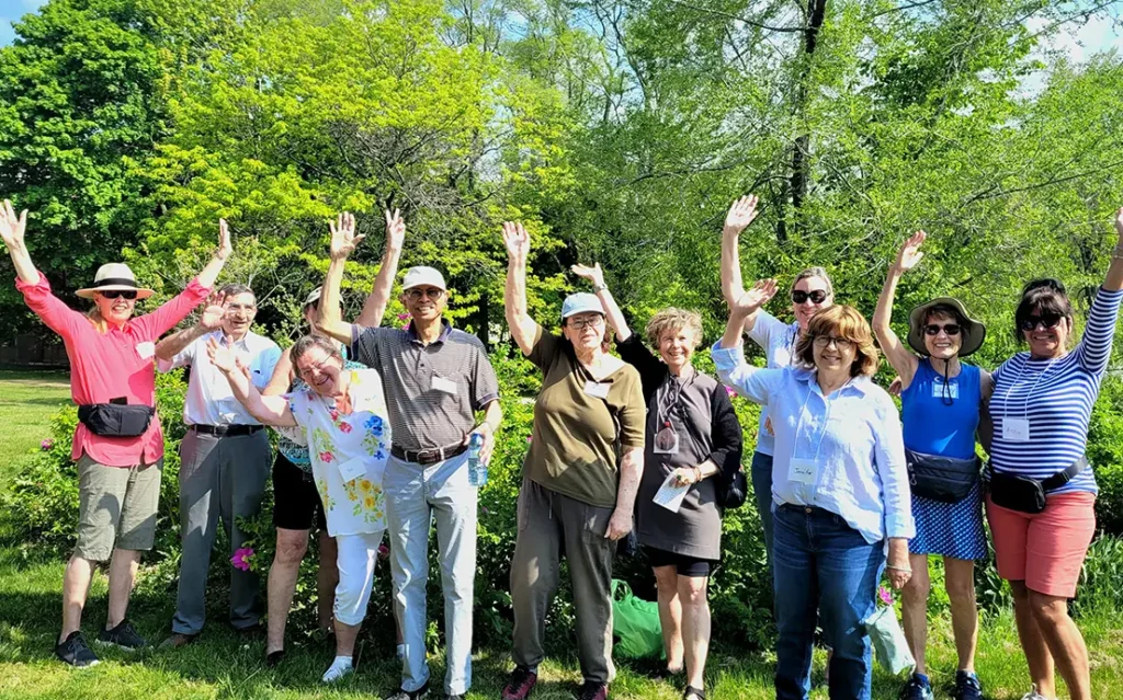Members of the Walking Through Grief group standing together smiling and raising their arms in from of trees in a park 