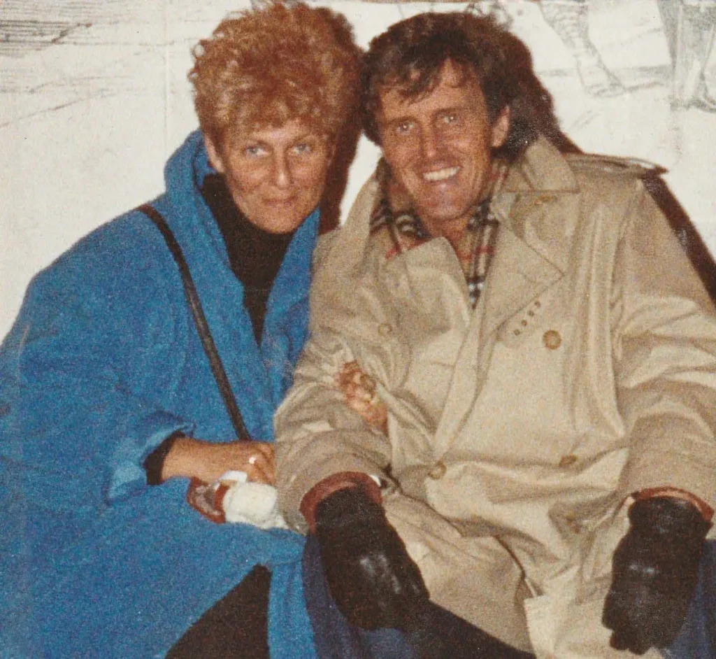 Ferne and Geoffrey sitting in front of a play billboard in London England.