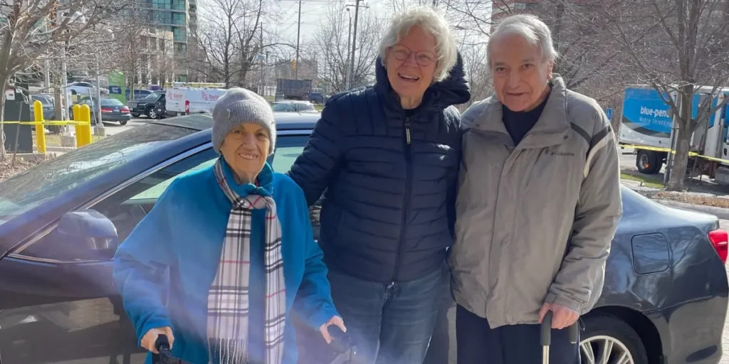 Dorothy Ley Hospice volunteer driver standing together with two day program clients in front of her vehicle.