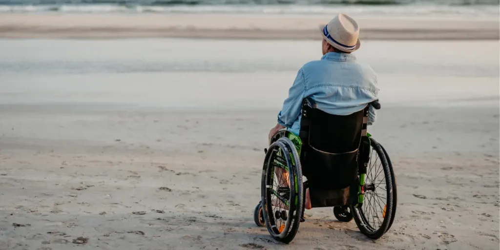 A man in a wheelchair on a beach looking out to the water